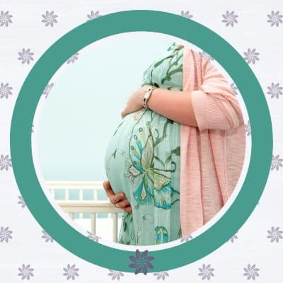 Woman holding pregnant belly in front of a crib