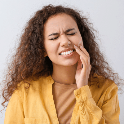 Woman with curly hair in yellow shirt, holding her jaw in pain, representing bleeding gums